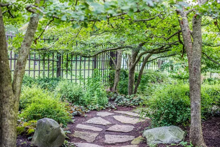 Curva de um caminho de pedras de um jardim, cercado por vegetaçãp.