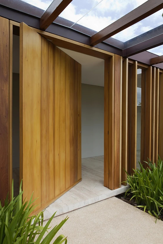 Hall de entrada com porta pivotante de madeira semi-aberta.