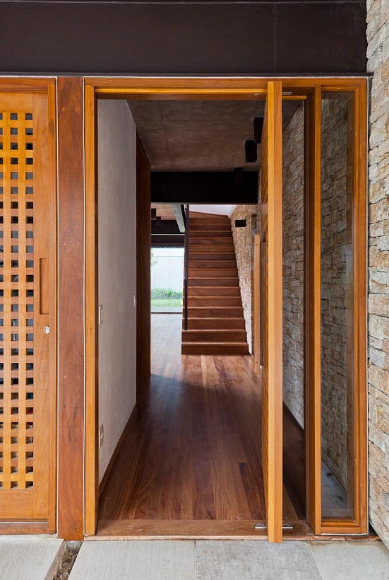 Hall de entrada com porta pivotante de madeira aberta.