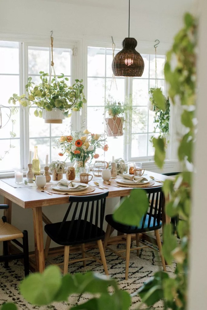 Mesa de jantar encostada em janelas. Várias plantas em vasos decoram o espaço.