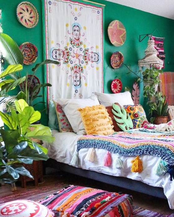 Quarto com parede de cabeceira verde. A cama é decorada por almofadas e colcha coloridas. Plantas fazem companhia à cama.