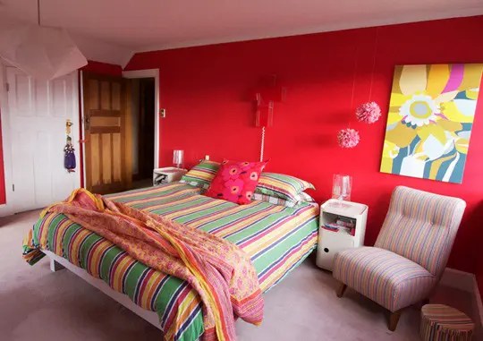 Quarto com parede de cabeceira vermelha e cama com colcha colorida.