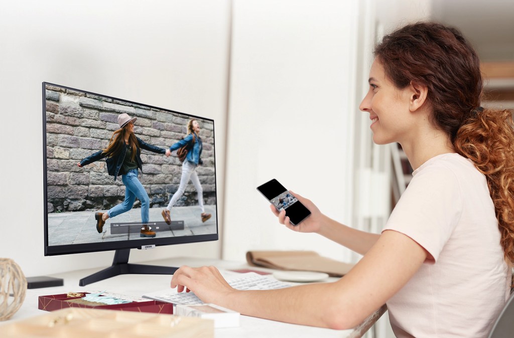 Mulher assiste a vídeo do celular com imagem espelhada no monitor Samsung M5.