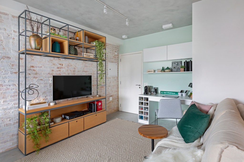 Sala de estar com um das paredes revestida com tijolos aparentes, Uma leve camada de tinta branca dá acabamento aos tijolinhos.