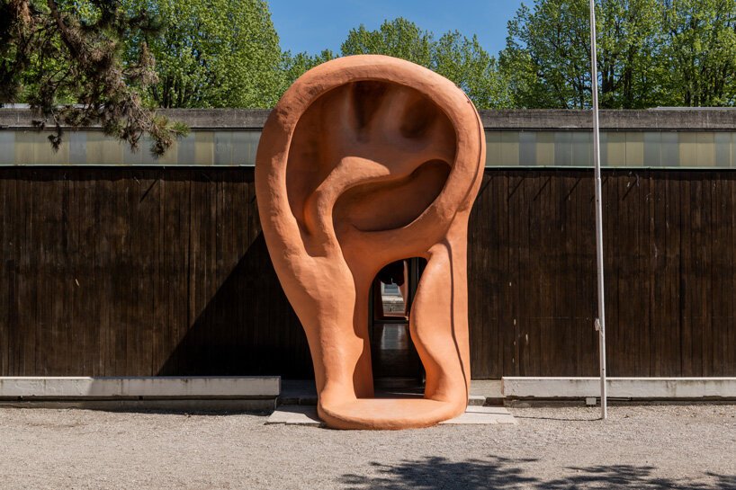Porta do pavilhão emoldurada por escultura de orelha gigante.