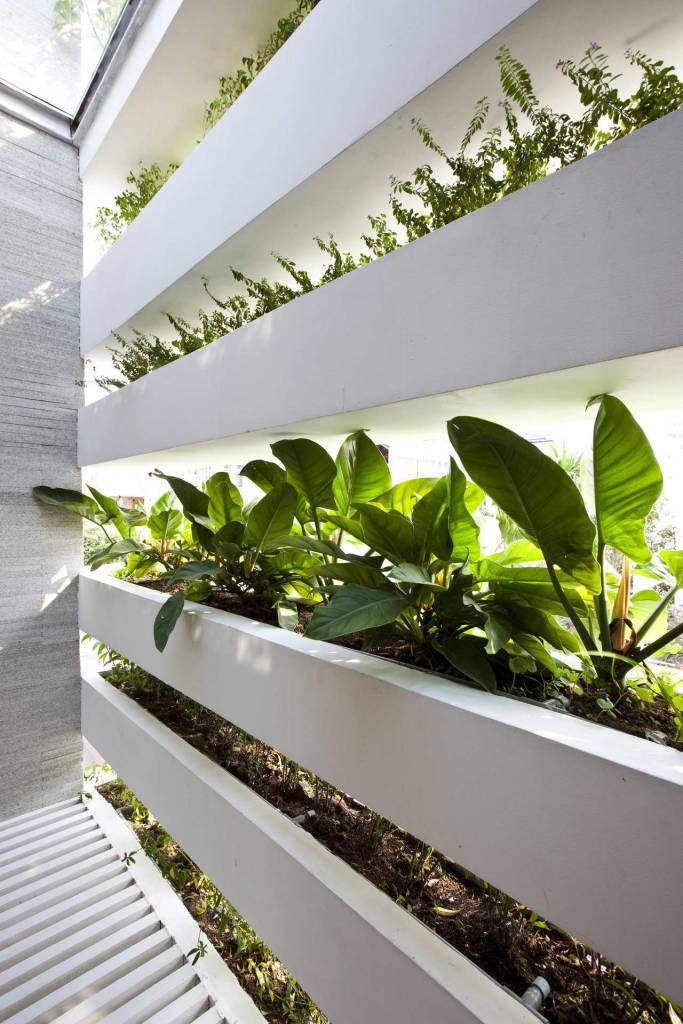 Foto mostra mais em detalhe as caixas de concreto na cor branca com plantas, que fazem o fechamento de toda a parede da casa.