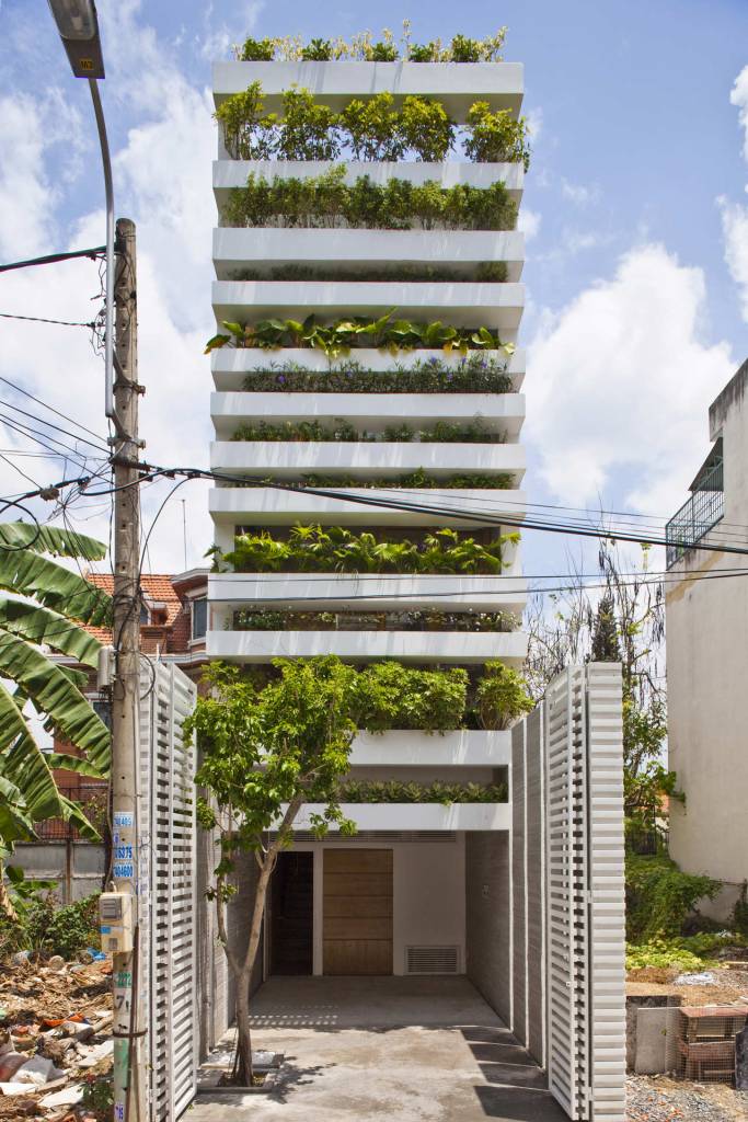 Foto mostra fachada de casa em terreno estreito, com alguns pavimentos em que se vê caixas de concreto com plantas formando um enorme jardim vertical.