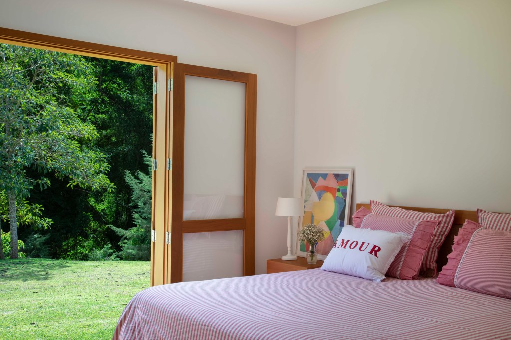 Quarto com cama de casal e roupa de cama cor de rosa com porta para o jardim