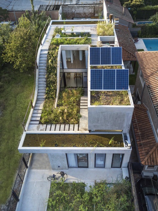 foto aérea mostra casa com telhados verdes e placas fotovoltaicas, com rampas e escadas integrando três pavimentos.
