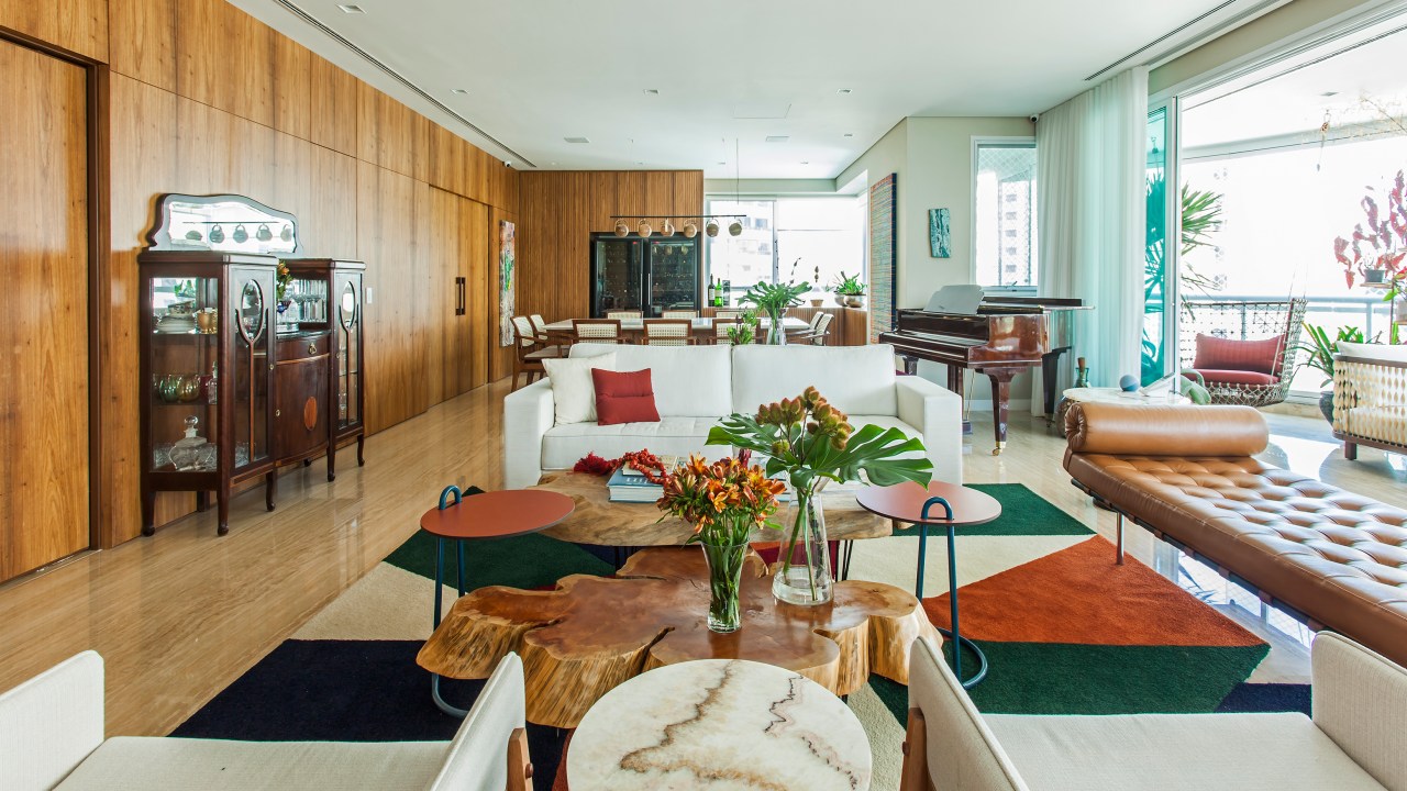Sala de estar com varanda integrada; tapete geométrico colorido; sofá branco e mesas de centro
