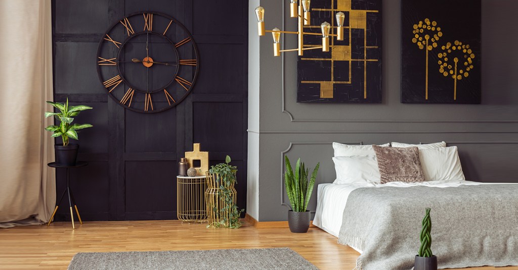 Quarto com paredes pretas e cinzas; piso em madeira; luminária dourada; relógio na parede