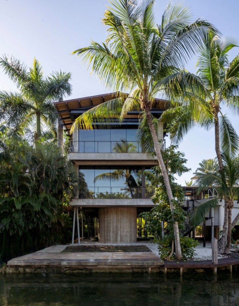Foto mostra casa suspensa por pilar delgado que sustenta dois pisos e cobertura em duas águas. Há palmeiras ao redor da construção.