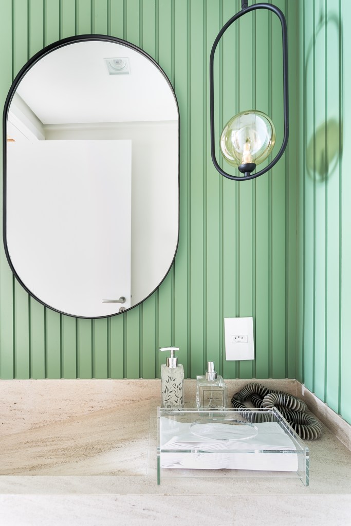 Lavabo com espelho oval; parede revestida de madeira ripada pintada de verde