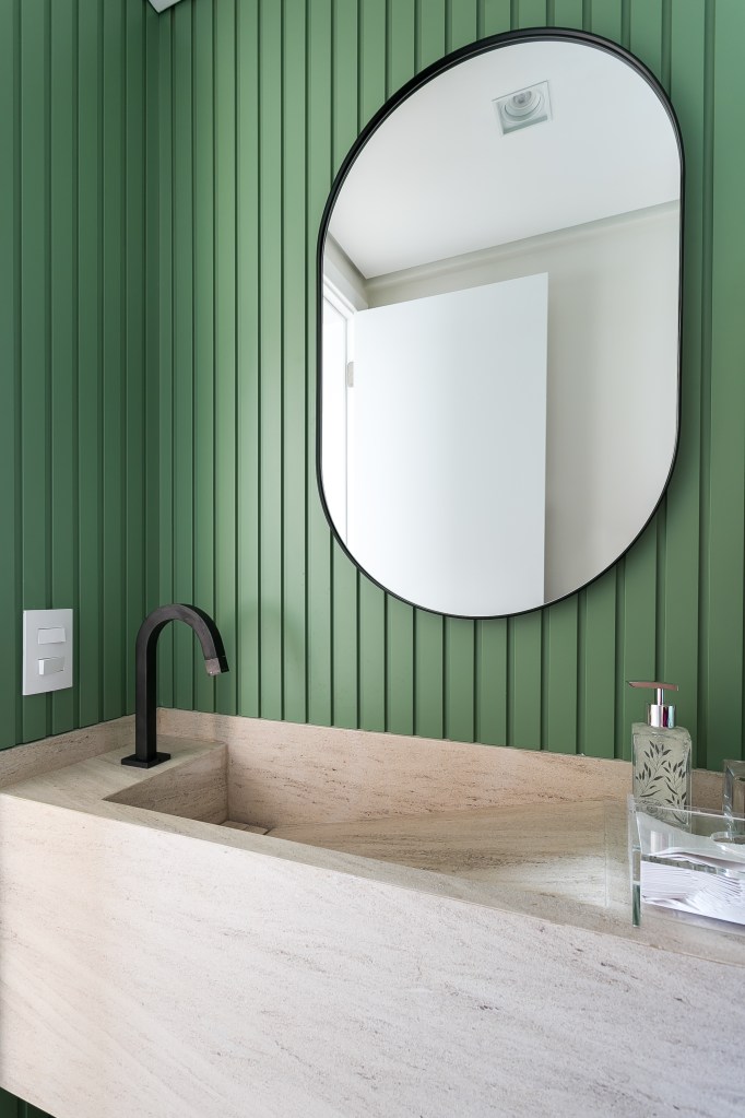 Lavabo com espelho oval; parede revestida de madeira ripada verde