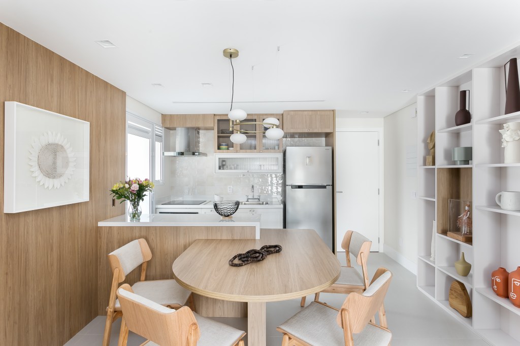 Sala integrada com cozinha; mesa de jantar em madeira; luminária; estante branca com nichos