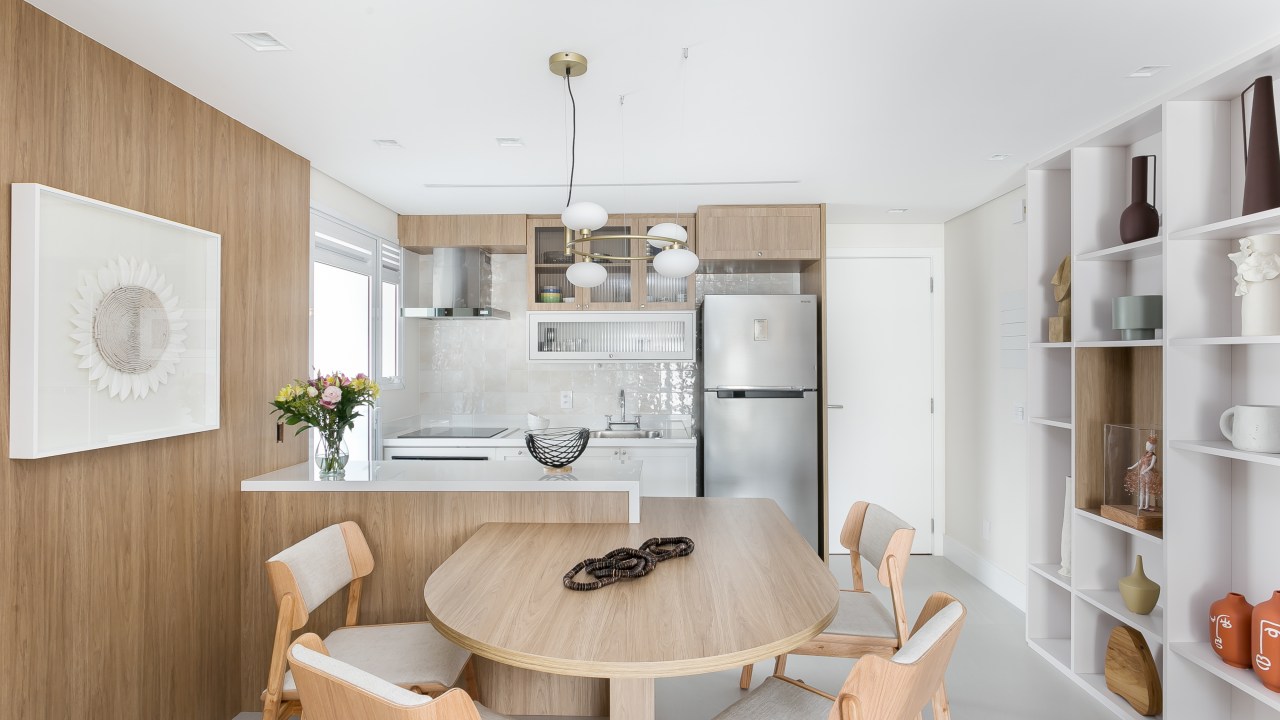 Sala integrada com cozinha; mesa de jantar em madeira; luminária; estante branca com nichos