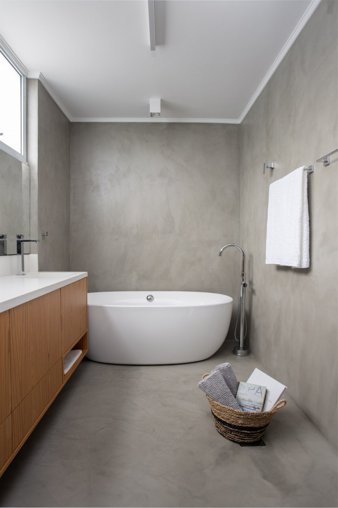 Banheiro com banheira solta; parede em cimento queimado