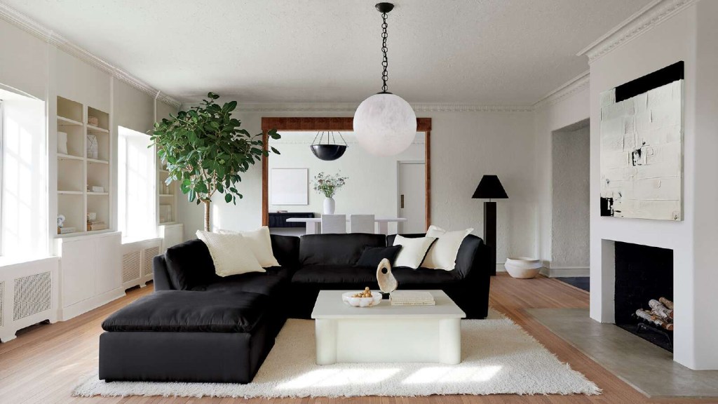 Sala de estar com sofá preto em formato L; mesa de centro branca; luminária esférica