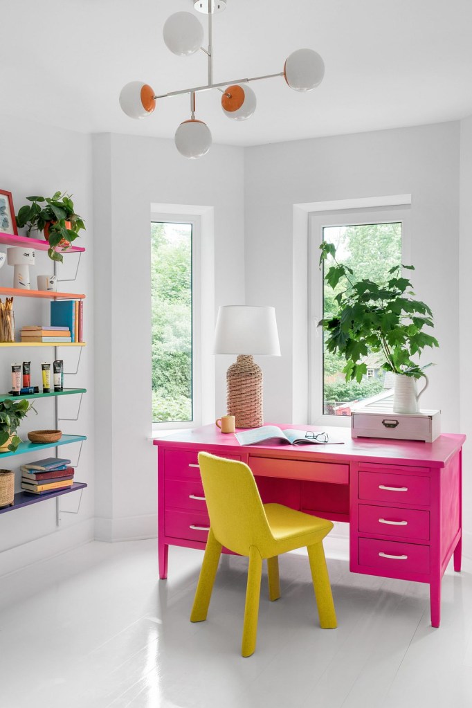10 home offices estilosos com plantas na decoração Big Country Built The Decoist Pequeno home office com boa iluminação natural. Teto, paredes e pisos em branco, com destaque de cor para a escrivaninha rosa e cadeira amarela. Uma planta decora a escrivaninha.