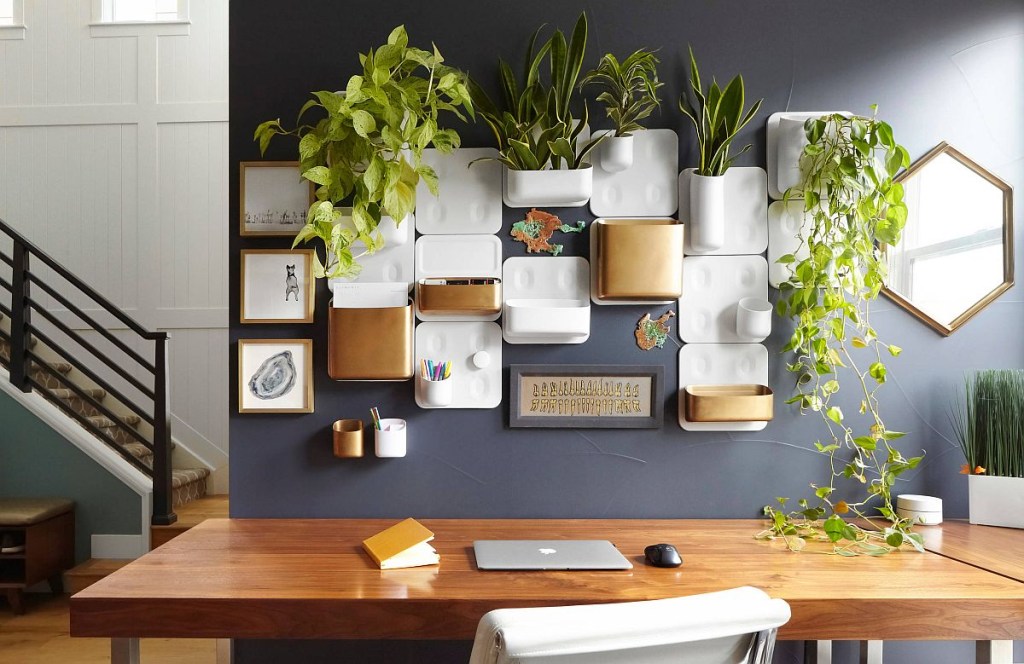 Home office com pequena mesa de madeira embutida na parede. Nesta mesma parede, vasos de plantas formam um jardim vertical reduzido.