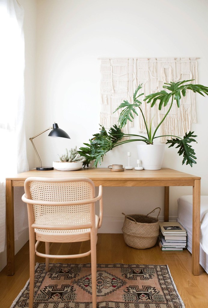 Home office minimalista com cadeira e mesa em madeira clarinha. Uma planta faz a decoração sobre a mesa.