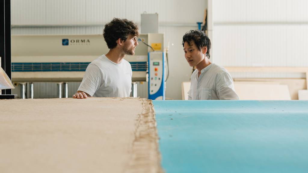 Foto mostra dois homens em frente a uma mesa onde se vê placas de papel.