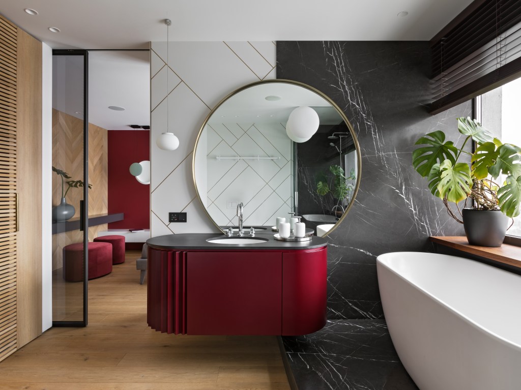 Banheiro luxuoso, com pia preta, armário vermelho e banheira apoiada em grande mármore preto.