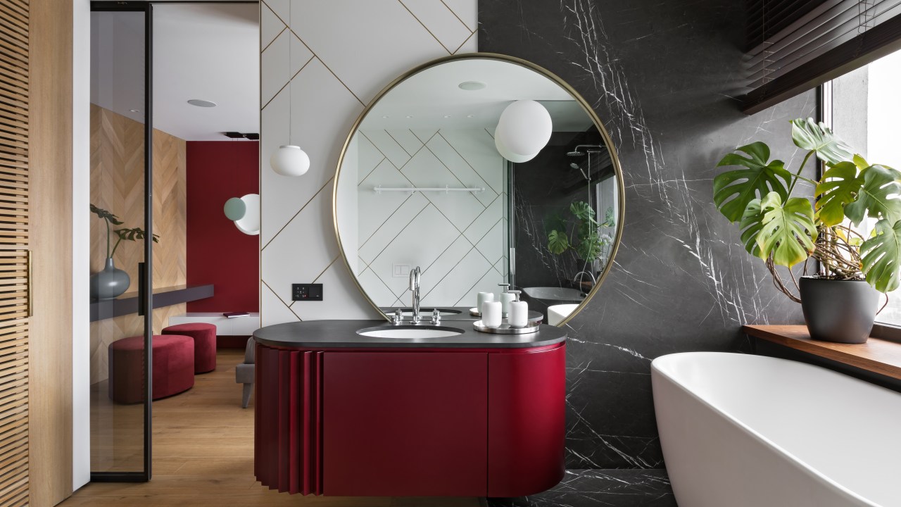 Banheiro luxuoso, com pia preta, armário vermelho e banheira apoiada em grande mármore preto.