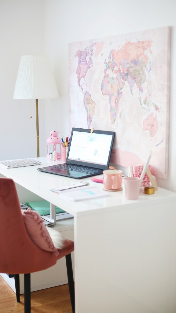Foto mostra escrivaninha em quarto que sugere ser de uma menina ou adolescente. Na mesa branca há um laptop e objetos cor de rosa.