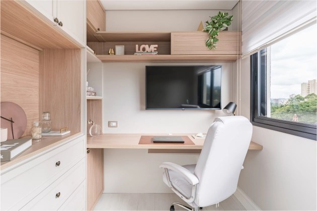 Foto mostra home office com armários e tampo de mesa em madeira clara e cadeira de escritório na cor branca.