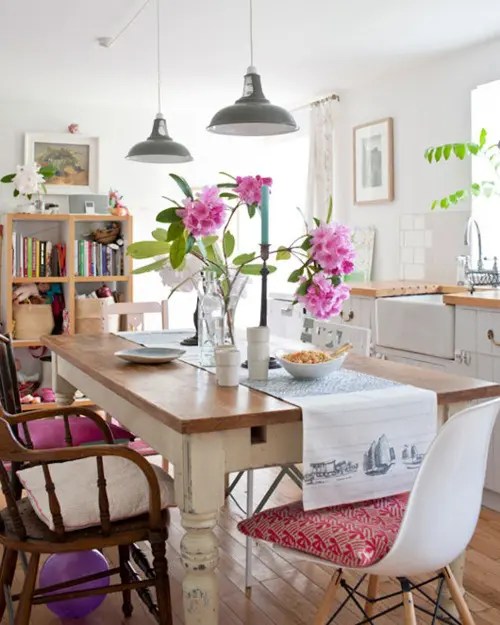 Sala de jantar com mesa e cadeiras de madeira. Flores decoram a mesa.