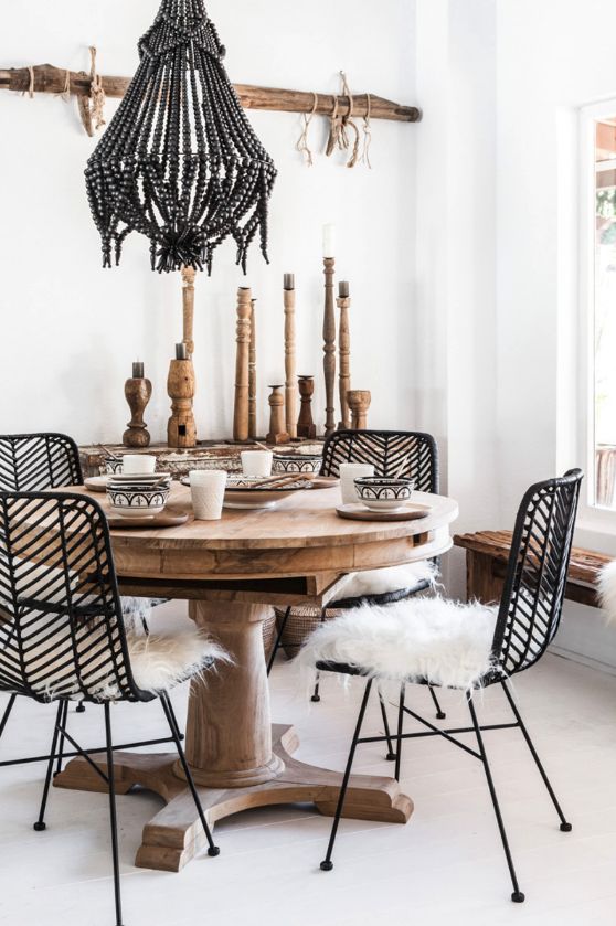 Sala de jantar com mesa redonda de madeira. Cadeira pretas de vime têm acolchoado felpudo branco.