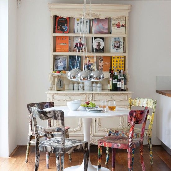 Sala de jantar com esa redonda branca e quatro cadeiras de madeira com diferentes padrões de pintura.