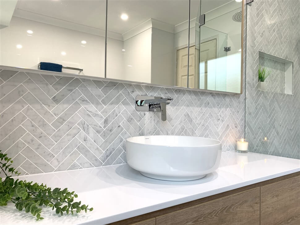 Backsplash de banheiro revestido com azulejos em padrão de espinha de peixe - os azulejos formam Vs.