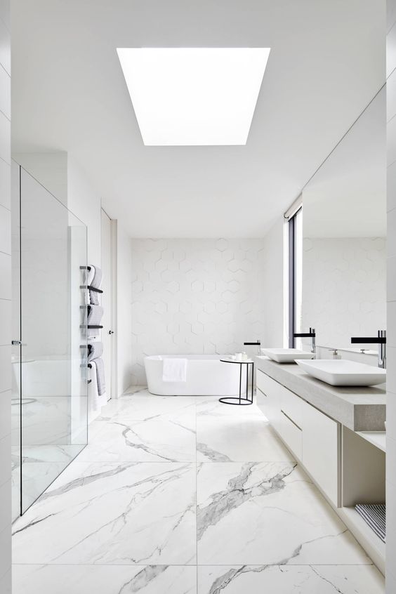 Banheiro minimalista todo em branco. O piso é revestido com pedras que apresentam uma textura em cinza clarinho.