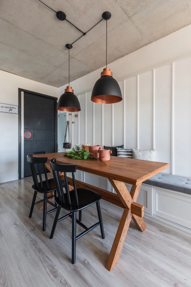 Foto mostra área de refeições em cozinha com piso laminado de madeira, mesa de madeira, banco em alvenaria revestida de lambri e duas cadeiras pretas.