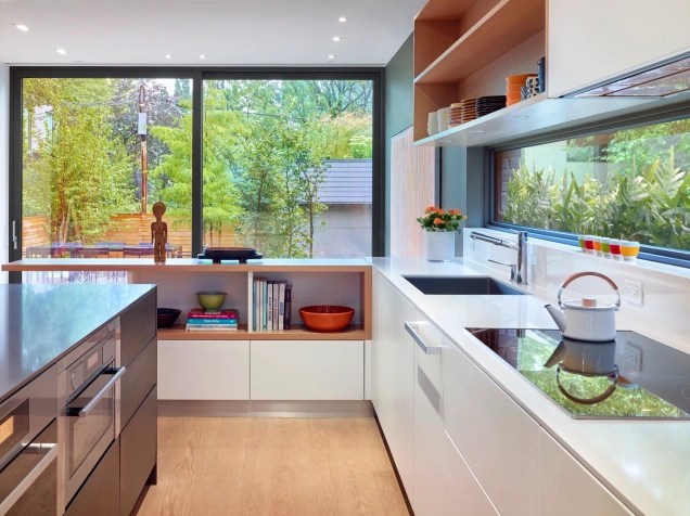 Foto mostra cozinha com piso vinílico que imita madeira, bancada de trabalho e aberturas de vidro que permitem vistas para o jardim externo.