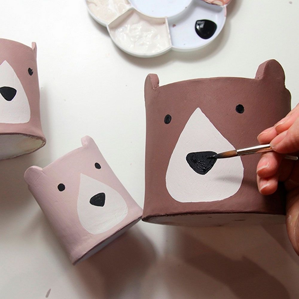 Rostos de ursinhos sendo pintados em vasinhos.