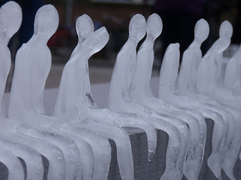 Pequenas esculturas de gelo derretendo de pessoas sentadas uma ao lado da outra de cabeças levemente baixas.