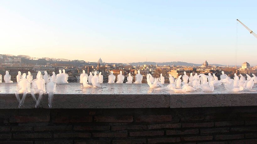 Pequenas esculturas de gelo derretendo de pessoas sentadas uma ao lado da outra de cabeças levemente baixas ao pôr do sol.