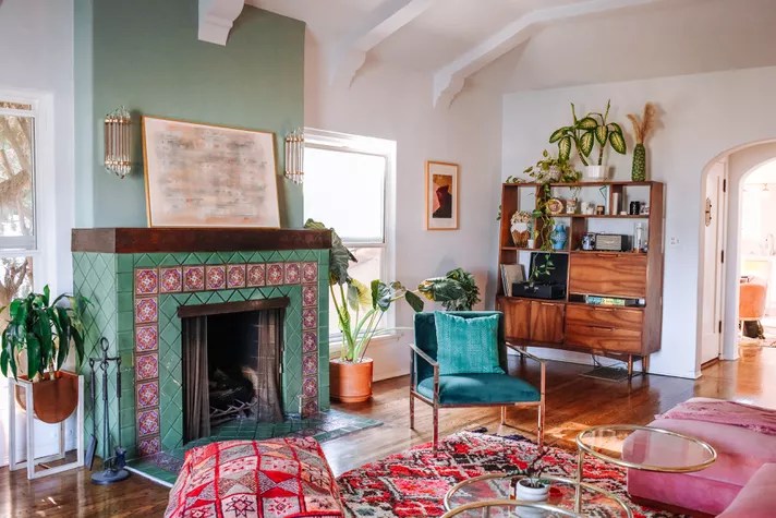 Ostentação veja 8 paletas de cor inspiradas em joias Dazey Den Sala de estar com uma parede de destaque verde, móveis, almofadas e tapetes em cores fortes.