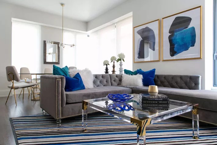 Sala de estar com tapete listrado, sofá cinza e almofadas coloridas.