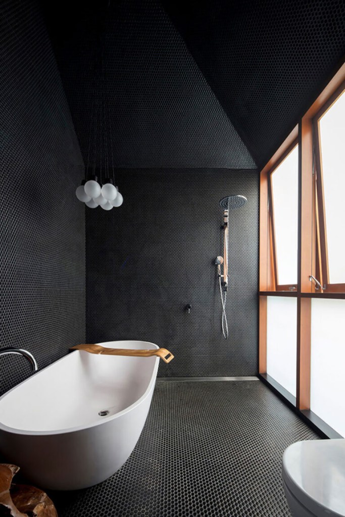 Banheiro com paredes teto e chão pintados de preto, com exceção de uma das paredes que é toda em vidro fosco com janelas na parte superior.