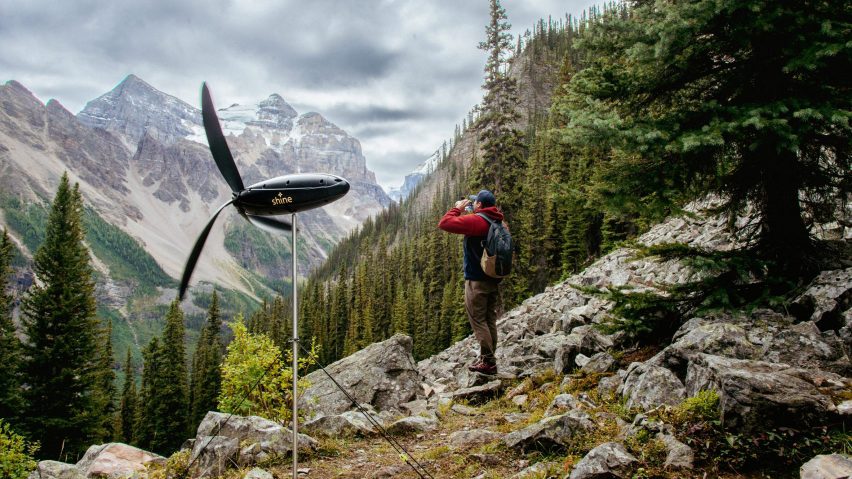 Turbina do tamanho de uma garrafa de 1 litro sobre um tripé metálico em meio a uma paisagem montanhosa.