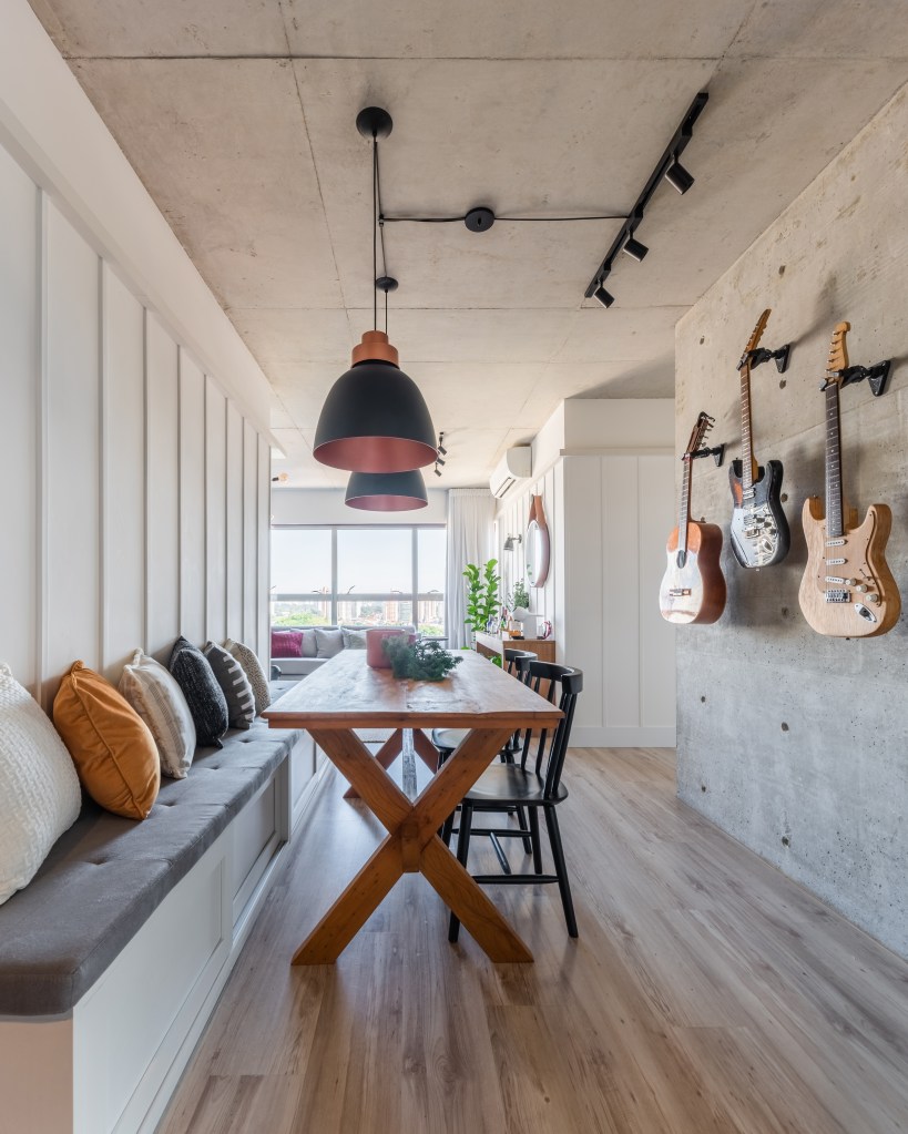 Sala de jantar com mesa em madeira e banco. Guitarras e violão pendurados na parede