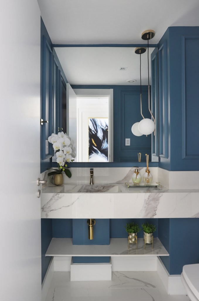Lavabo com bancada em mármore; paredes azuis; luminária esférica ao lado de espelho