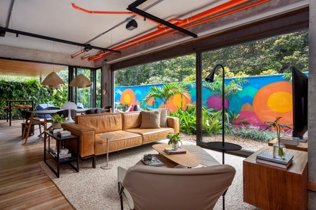 Foto mostra sala de estar com tubulação aparente nas cores preto e laranja, compondo o décor.
