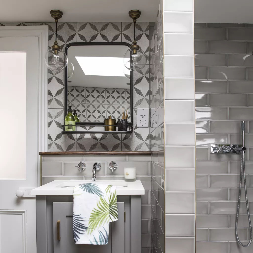 Banheiro com azulejos cinzas, u m pequeno espelho e duas luminárias penduradas.