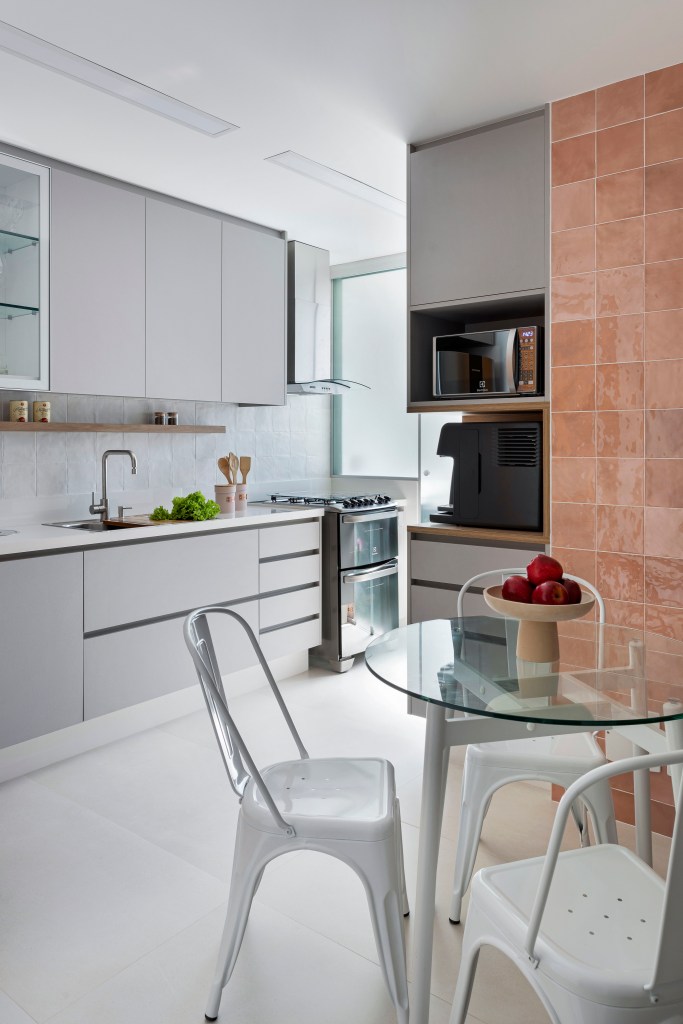 Cozinha com armários cinza; mesa pequena redonda com tampo de vidro para refeições