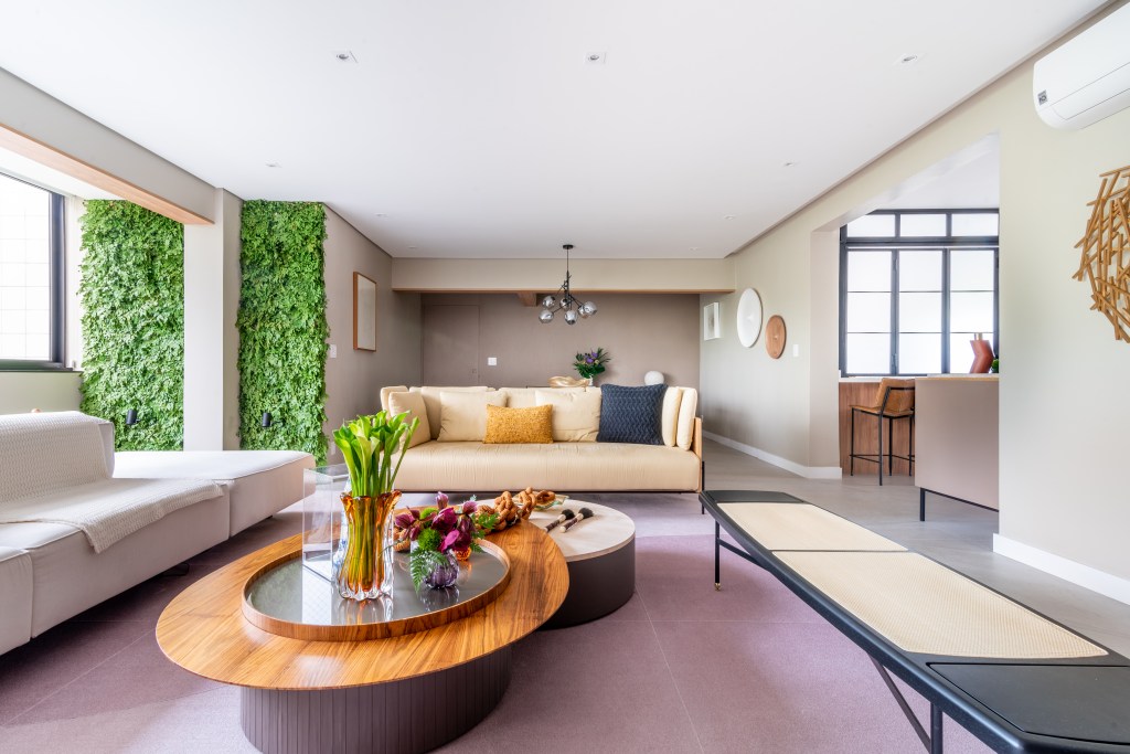 Sala de estar com sofá, mesa de centro oval e banco; jardim vertical ao fundo